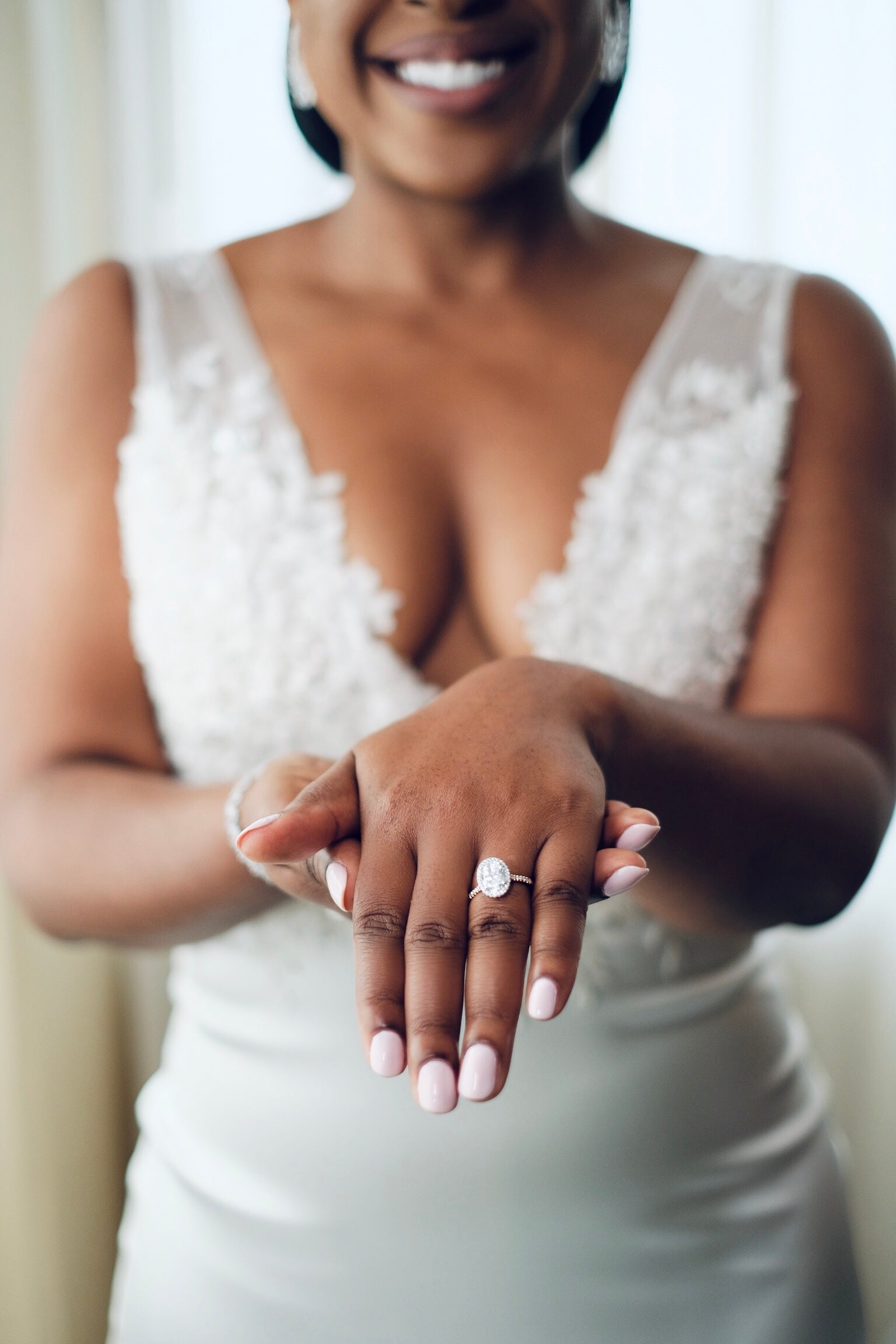 Black bride in a white fitted v neck wedding dress showing off her 3 carat oval engagement with a halo and gold pave band.